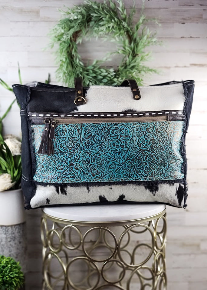 Turquoise Patina Cowhide Weekender Bag on white table with green decor