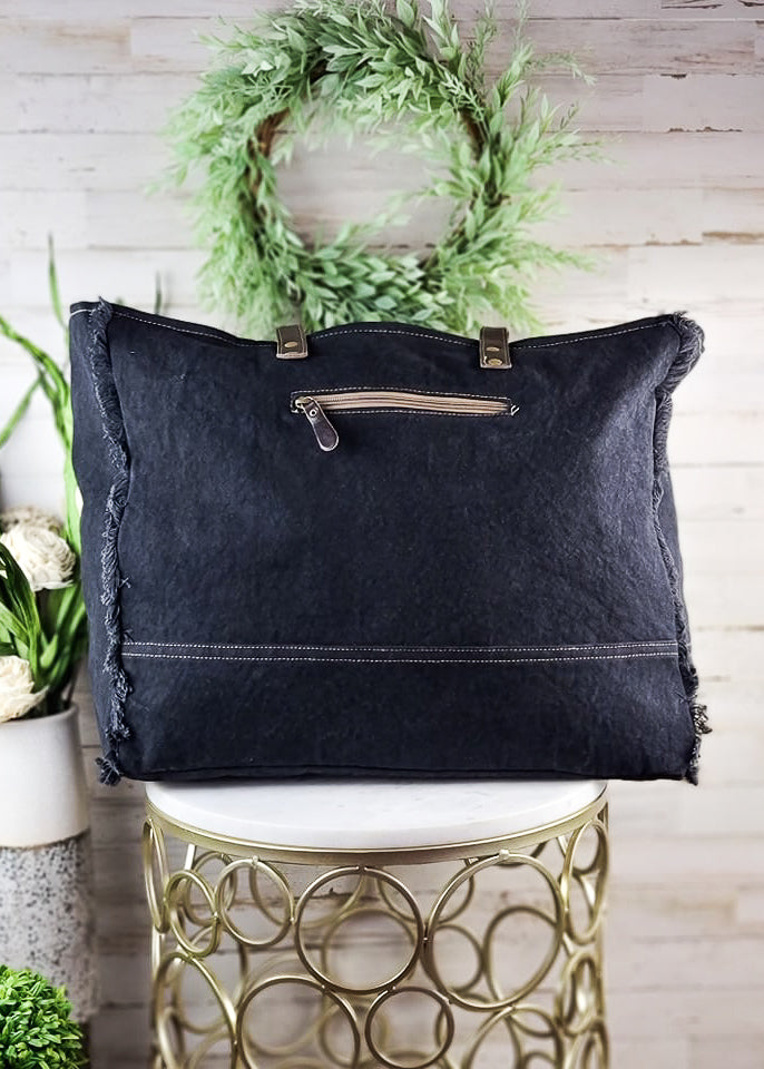 Turquoise Patina Cowhide Weekender Bag on white table with green decor, back view
