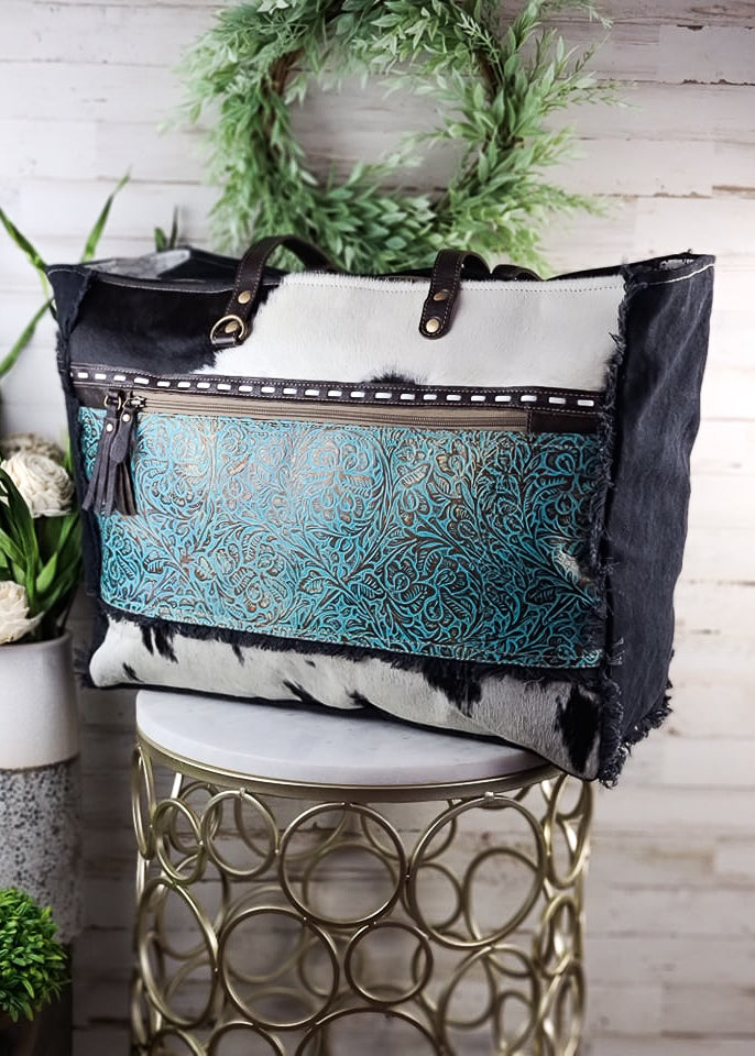 Turquoise Patina Cowhide Weekender Bag on white table with green decor