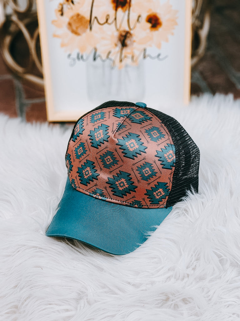 Dark teal hat bill with brown and teal aztec trucker cap with mesh back. Sits on faux fur rug making the colors vibrant..