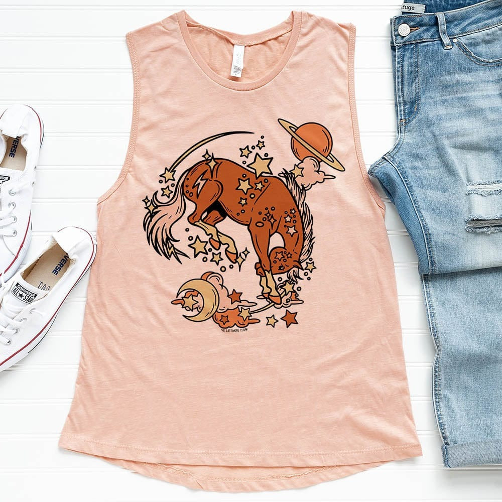 Heather peach tank top with cosmic orange horse and star design. Tank lays on white background with distressed jeans and white converse. 