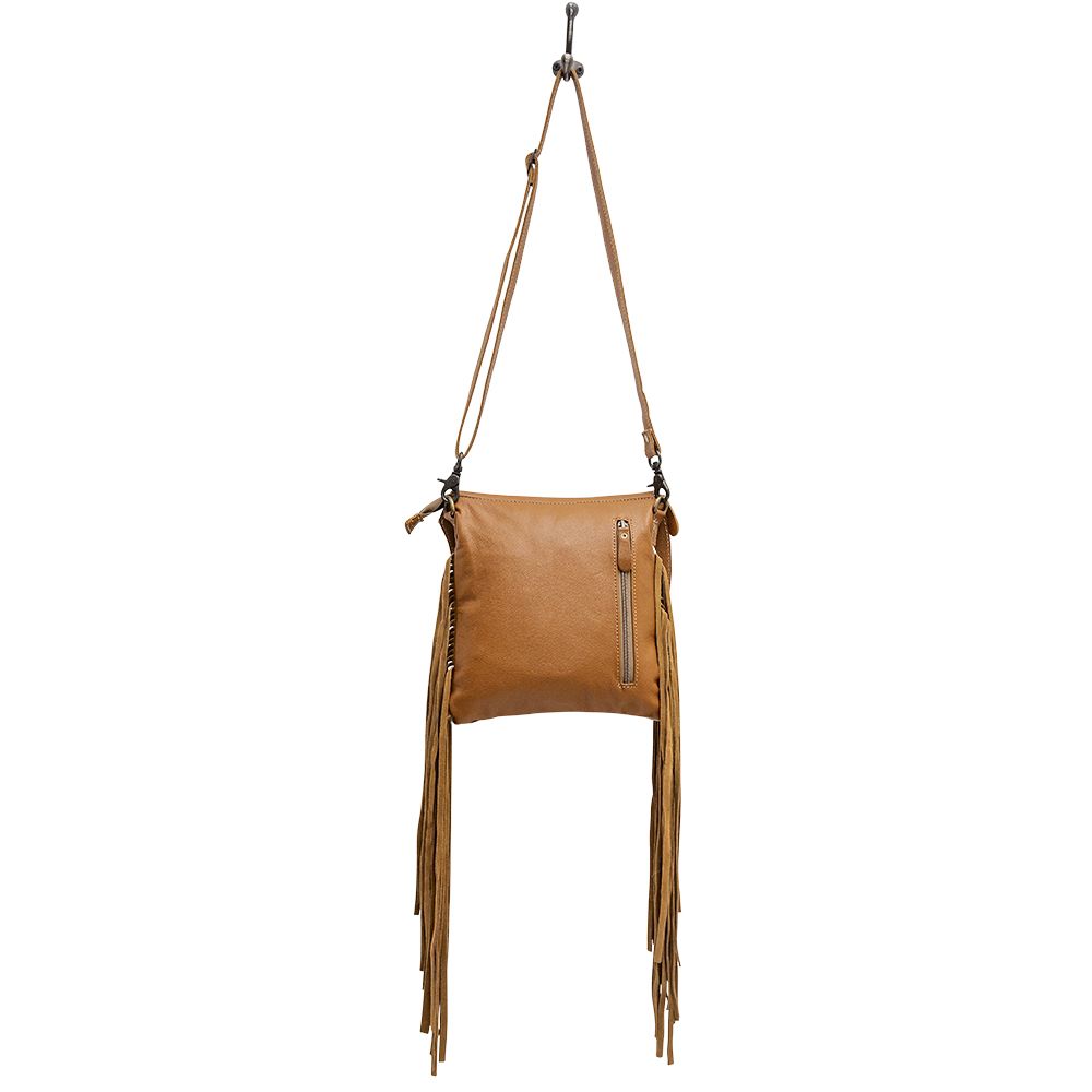 Backside of fringe cowhide purse hangs from white background. Back zippered conceal pocket. 